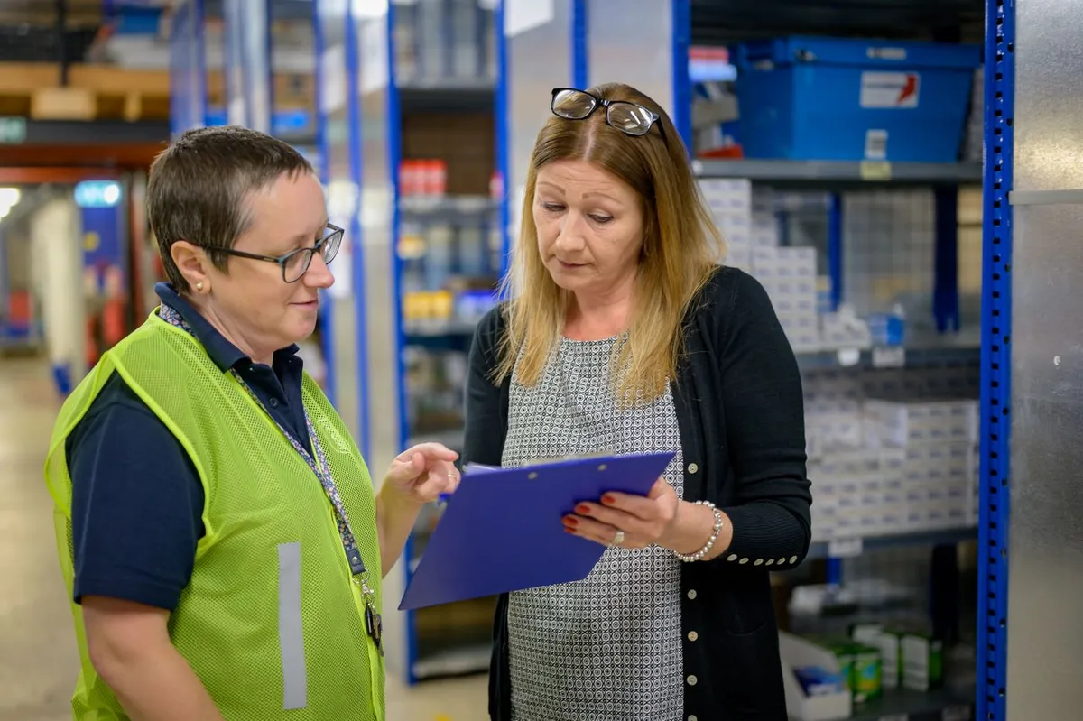 Two people review tracking paperwork in a storage space.